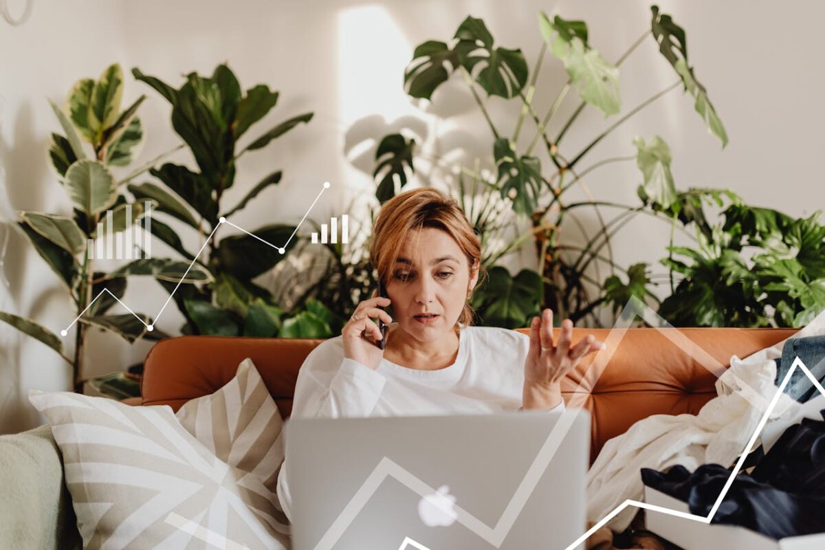 Woman multitasking on phone and laptop, analyzing data charts, surrounded by greenery.